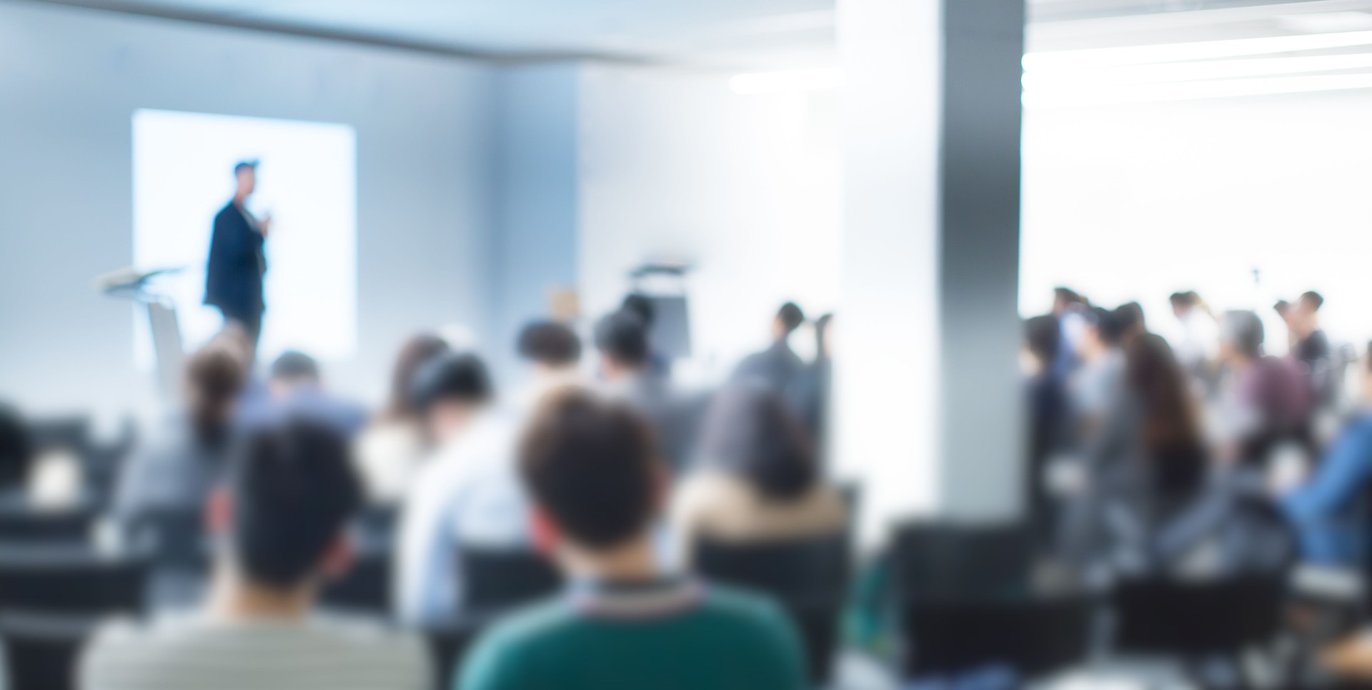 Blurred De-focused Audience in Conference Lecture Presentation Room. Corporate Presentations in Conference Hall. Seminar Speaker Giving Training to New Employees. Blurred  Hip Presenter wearing Hat.